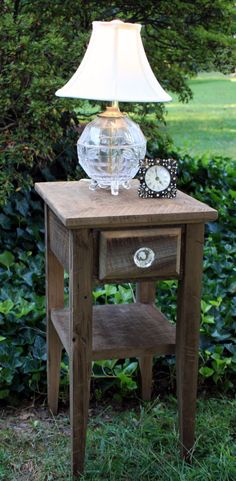 a small wooden table with a glass lamp on top and a clock sitting on it