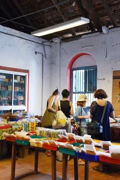 three women standing at a table with food on it in front of a store window