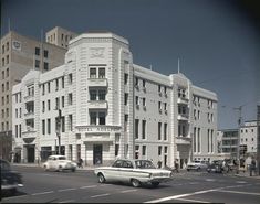 an old photo of cars driving down the street in front of a large white building