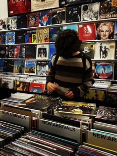 a woman standing in front of a wall full of records and cds on display at a record store