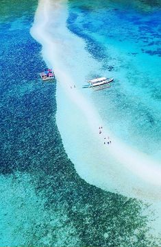 two boats floating on top of a body of water next to shore covered in sand