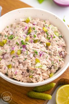 a white bowl filled with tuna salad on top of a wooden cutting board next to sliced cucumbers