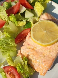 a piece of salmon on a plate with lettuce, tomatoes and lemon wedges