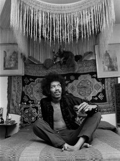 a man sitting on top of a bed in a room filled with rugs and pictures