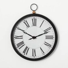 a black and white clock with roman numerals on it's face is hanging from the wall