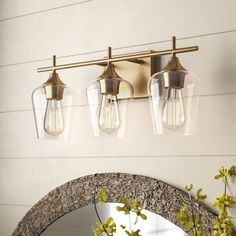 three light bathroom fixture with clear glass shades on the wall and gold fixtures above it