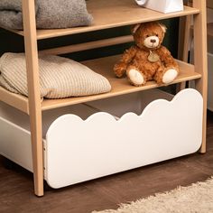 a brown teddy bear sitting on top of a wooden shelf next to pillows and blankets