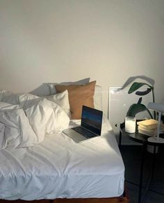 a laptop computer sitting on top of a bed with white sheets and pillows in a bedroom