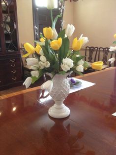 a vase filled with yellow and white tulips on top of a wooden table