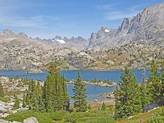 a mountain lake surrounded by trees and rocks with mountains in the backgrouds