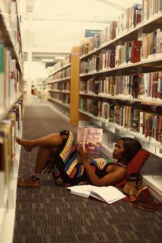 a woman sitting on the floor reading a book in front of a row of bookshelves