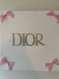 the word dior is made out of metal letters with pink bows around it and on top of a white canvas