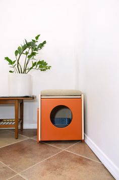 an orange box sitting on the floor next to a table with a plant in it