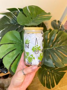 a person holding up a jar with plants in it next to a potted plant