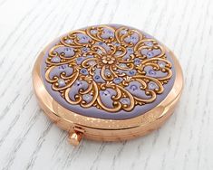 a close up of a small purple and gold pocket watch on a white table top