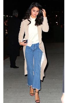 a woman walking down the street at night wearing high waist jeans and a trench coat