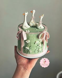 a hand holding a cake decorated with ducks and daisies in pastel green frosting