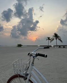 a bicycle is parked on the beach with palm trees and clouds in the sky behind it