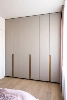 an empty bedroom with white closets and pink curtains on the windowsill, next to a bed