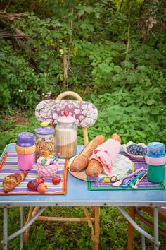 a picnic table with food on it in front of some trees and bushes, along with an umbrella