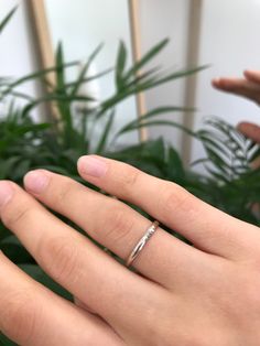 a woman's hand with a wedding ring on top of her finger next to a potted plant