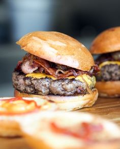 two hamburgers sitting on top of a wooden table next to small slices of pizza