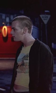 a man standing in front of a red car on the street at night with his head turned to the side