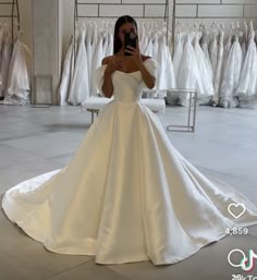 a woman taking a selfie while wearing a wedding dress in a bridal gown shop