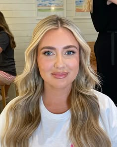 a woman with long blonde hair sitting in front of a mirror and looking at the camera