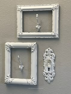 two white frames are hanging on the wall next to an ornate clock and keyhole