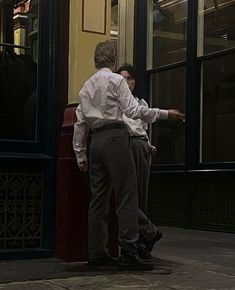 two men are standing in front of a window and one man is pointing at something