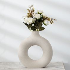 a white vase with flowers in it sitting on a table