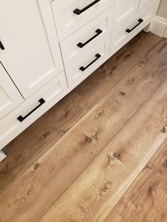 a kitchen with white cabinets and wood flooring on the counter top, along with black handles