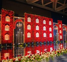 an elaborately decorated stage with red flowers and greenery on the sides, reflecting in water