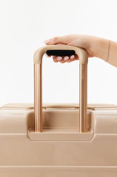 a woman's hand holding on to a beige piece of luggage that is in front of a white background