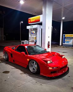 a red sports car parked in front of a gas station at night with its lights on