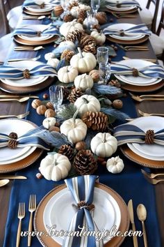 the table is set with blue and white plates, silverware, pine cones, and pumpkins