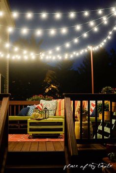 an outdoor deck with lights strung over it and pillows on the couches under them