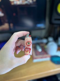 a hand holding a small toy with an evil face on it in front of a television