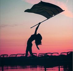 a woman holding a flag while standing on top of a body of water at sunset