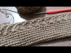 the yarn is being used to make a knitted scarf with red handled crochet hooks