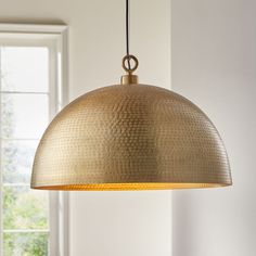 a large brass pendant light hanging from a ceiling fixture in a white room with windows