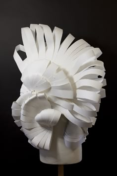 a sculpture made out of white paper on top of a wooden stick in front of a black background