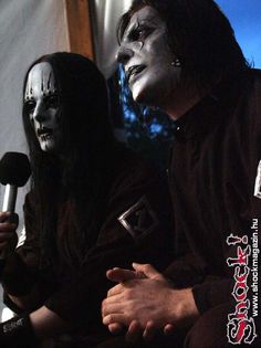 two people with black face paint on their faces and one holding a microphone in front of them