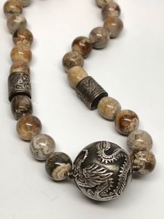 Wonderful necklace with a large silver bead feature 2 Chinese dragons. There are also 2 barrel shaped silver beads with birds and flowers on them. The stone beads are a brown and beige agate, each one is unique with swirls of different colors. The clasp is a large oval marked sterling. Each bead is hand knotted. The barrel silver beads have some copper showing through, otherwise in great condition. Necklace measures 14 inches long. Dragon bead measures approximately 1 inch in diameter. Agate bea Silver Agate Beaded Necklace, Silver Agate Beaded Necklaces With Round Beads, Silver Agate Beaded Necklaces With Polished Beads, Silver Agate Beaded Necklace With Polished Beads, Silver Agate Jewelry With Large Beads, Unique Silver Beads With Natural Stones, Artisan Silver Agate Beaded Necklace, Unique Silver Agate Beaded Necklaces, Chinese Dragons