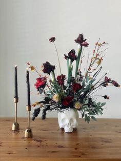 a vase with flowers and candles sitting on a table next to a candle holder in the shape of a skull