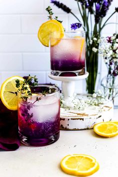 two glasses filled with purple lemonade sitting on top of a table next to flowers