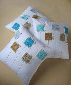 two white pillows with blue and brown crocheted squares on them sitting next to each other