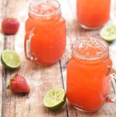 two mason jars filled with strawberry lemonade and limes next to strawberries on a wooden table