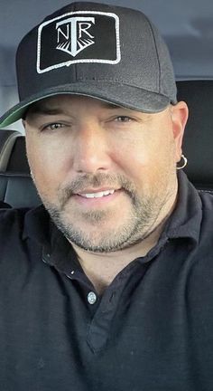 a man in a black shirt and hat sitting in the back seat of a car